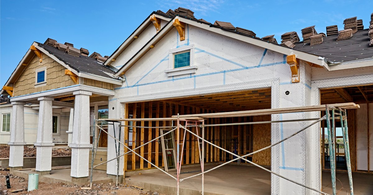 The frame of a house under construction with scaffolding and blue painter's tape on the home's façade.