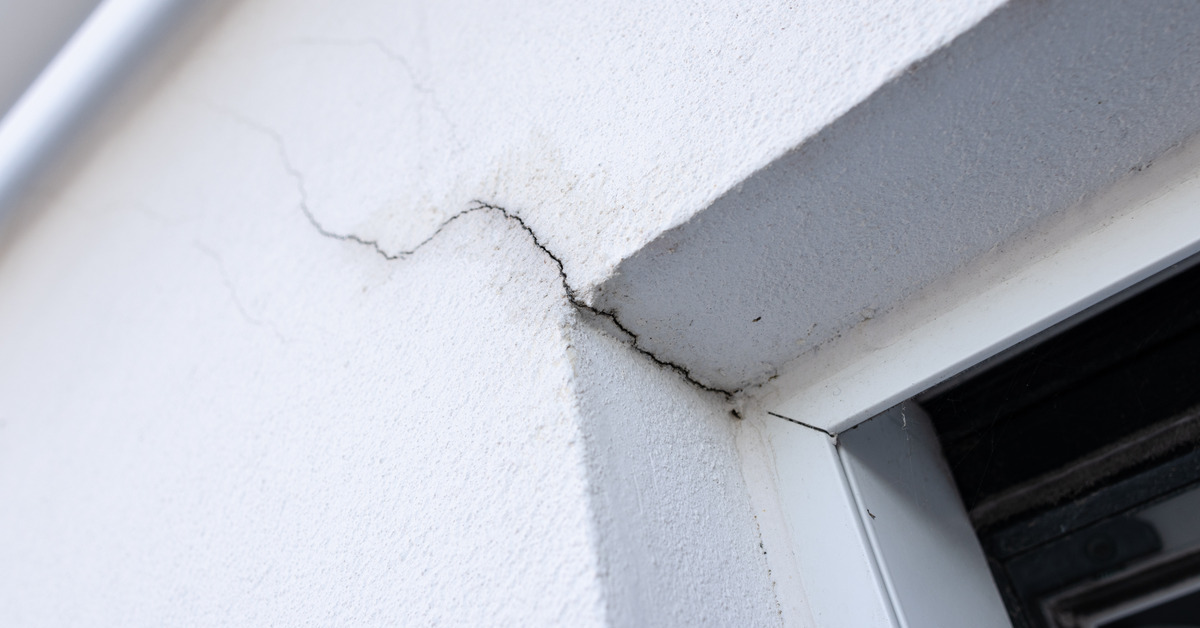 A white stucco wall with a deep crack running down it, the crack runs into the crook of a door frame.