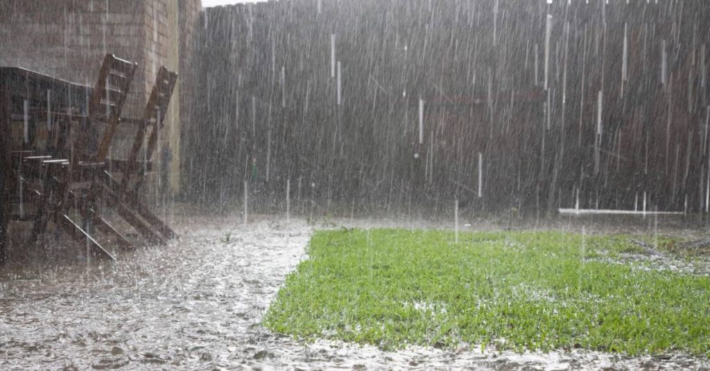 Heavy rain is coming down and pooling around the little bit of grass standing out on a residential property.