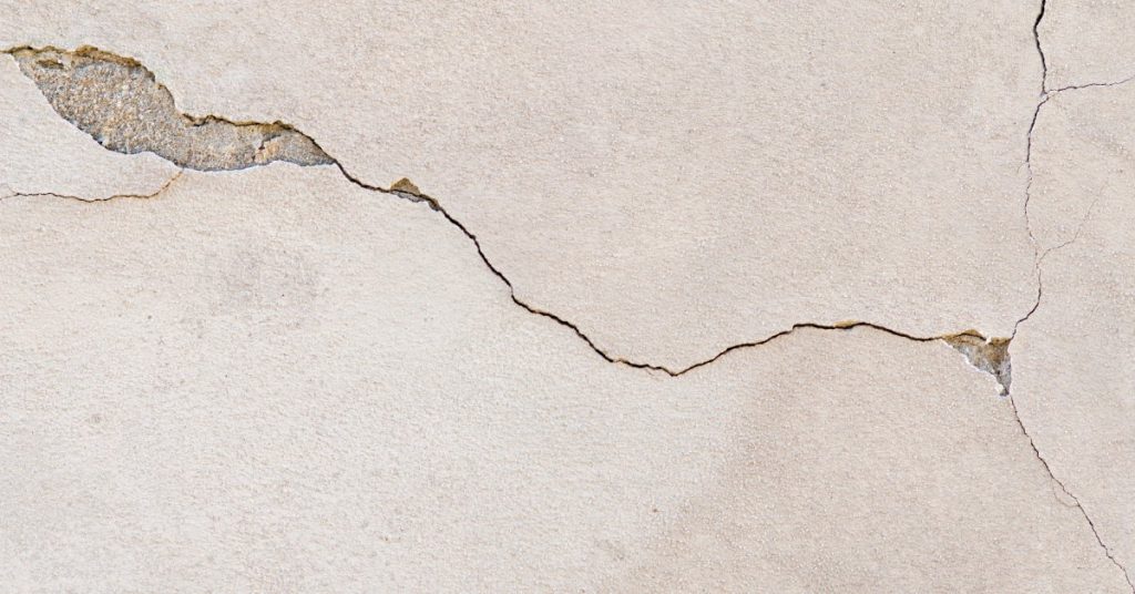 A close-up of stucco with a large, veiny crack running through it. Some parts of the crack are chipped away.