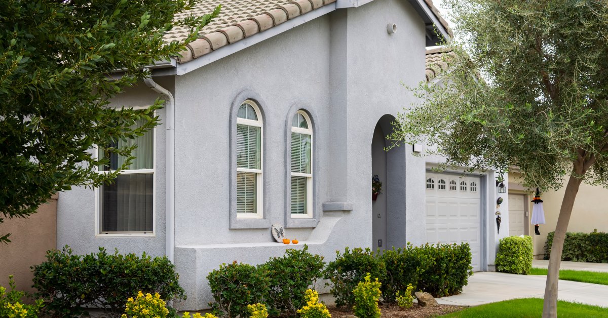 A suburban home with pale blue stucco walls, neat landscaping, small trees, and a clean tile roof.